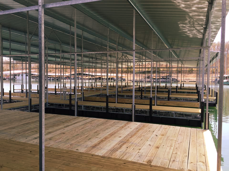 Interior perspective of an expansive, well-maintained covered boat dock featuring sturdy wooden decking walkways and rows of empty covered boat slips under a protective metal roof structure.