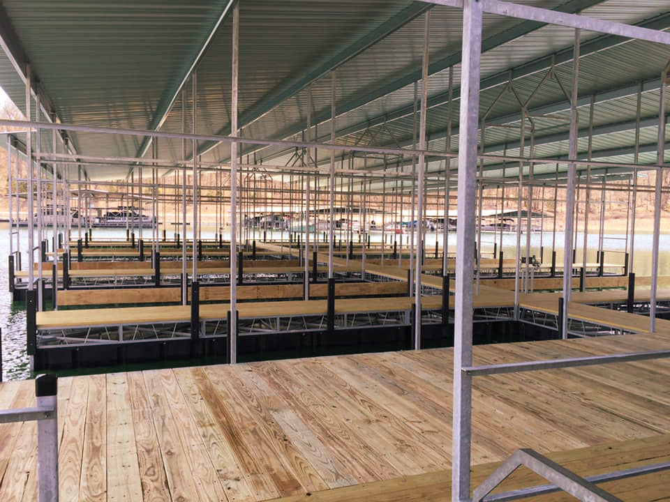 Interior perspective of an expansive, well-maintained covered boat dock featuring sturdy wooden decking walkways and rows of empty covered boat slips under a protective metal roof structure.